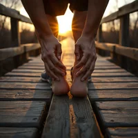 Two hands gripping bare feet and ankles on a wooden boardwalk, with low sun shining behind