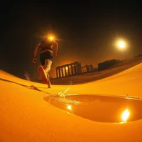 Fisheye view of a runner sprinting down a sand dune at night with bright lights illuminating the scene