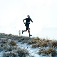 Runner in black kit running across a frost-covered hillside in misty winter conditions