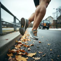 Runner's bare leg and shoe resting on a curb beside fallen autumn leaves and a metal railing on a road.