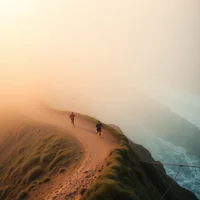 Aerial shot of three runners jogging on foggy coastal trail at dawn with ocean views
