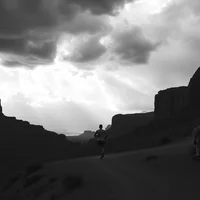 Person silhouetted against dramatic cloudy sky in rocky canyon landscape