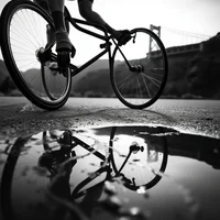 Black and white low-angle shot of cyclist on road bike with puddle reflection on wet asphalt