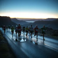 Group of runners on a wet mountain road at dawn, with misty valleys and rocky cliffs behind them.