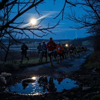 Group of runners and walkers moving along a hilly path at night under a bright moon, mixing running and walking