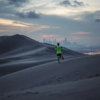 Runner in neon yellow-green top on a sandy dune ridge at dusk, with a city skyline glowing on the horizon