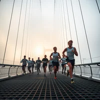 Diverse race pack in monochrome gear crossing a foggy suspension bridge at mid-morning, showing visible exhaustion.