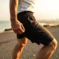 Runner in black shorts and white tank top, hand on hip, on a seaside asphalt path in warm light.