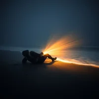 Motion-blurred para-athlete collapsed on misty winter shoreline, headlamp glowing in darkness, dwarfed by vast grey ocean.
