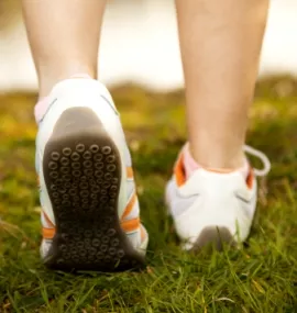 Rear view of a person's feet in white running shoes with orange accents, stepping across green grass