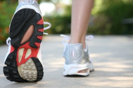 Close-up of a person walking on a paved path, showing the black, red and white sole of one running shoe